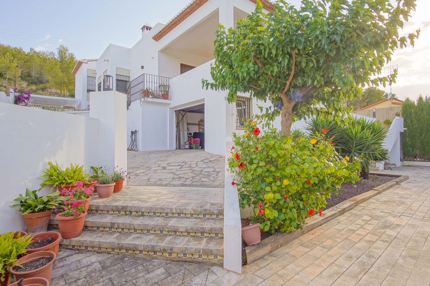 Außenansicht der Garageneinfahrt und des Souterrains mit Steintreppen, traditionellen Fliesenmustern und mediterraner Gartenanlage.