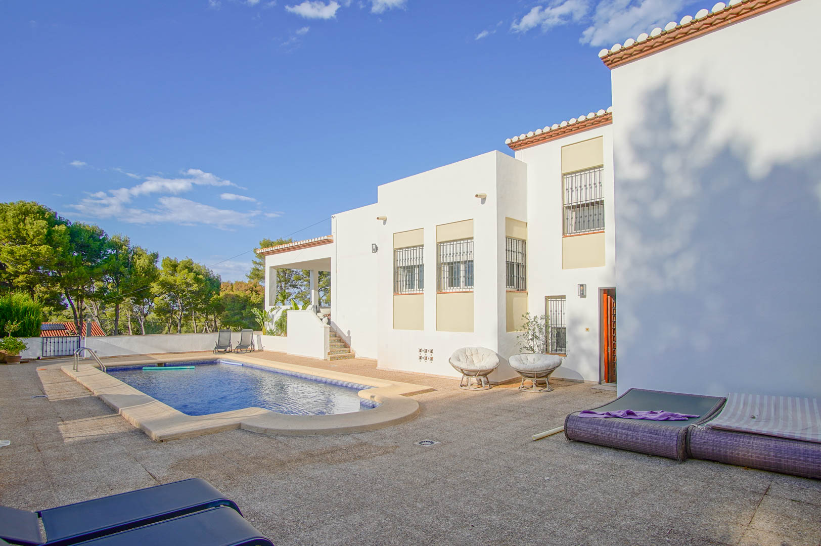 Außenansicht der weißen Villa mit privatem Pool und großzügiger gepflasterter Terrasse, eingebettet in eine mediterrane Umgebung mit Pinienbestand.