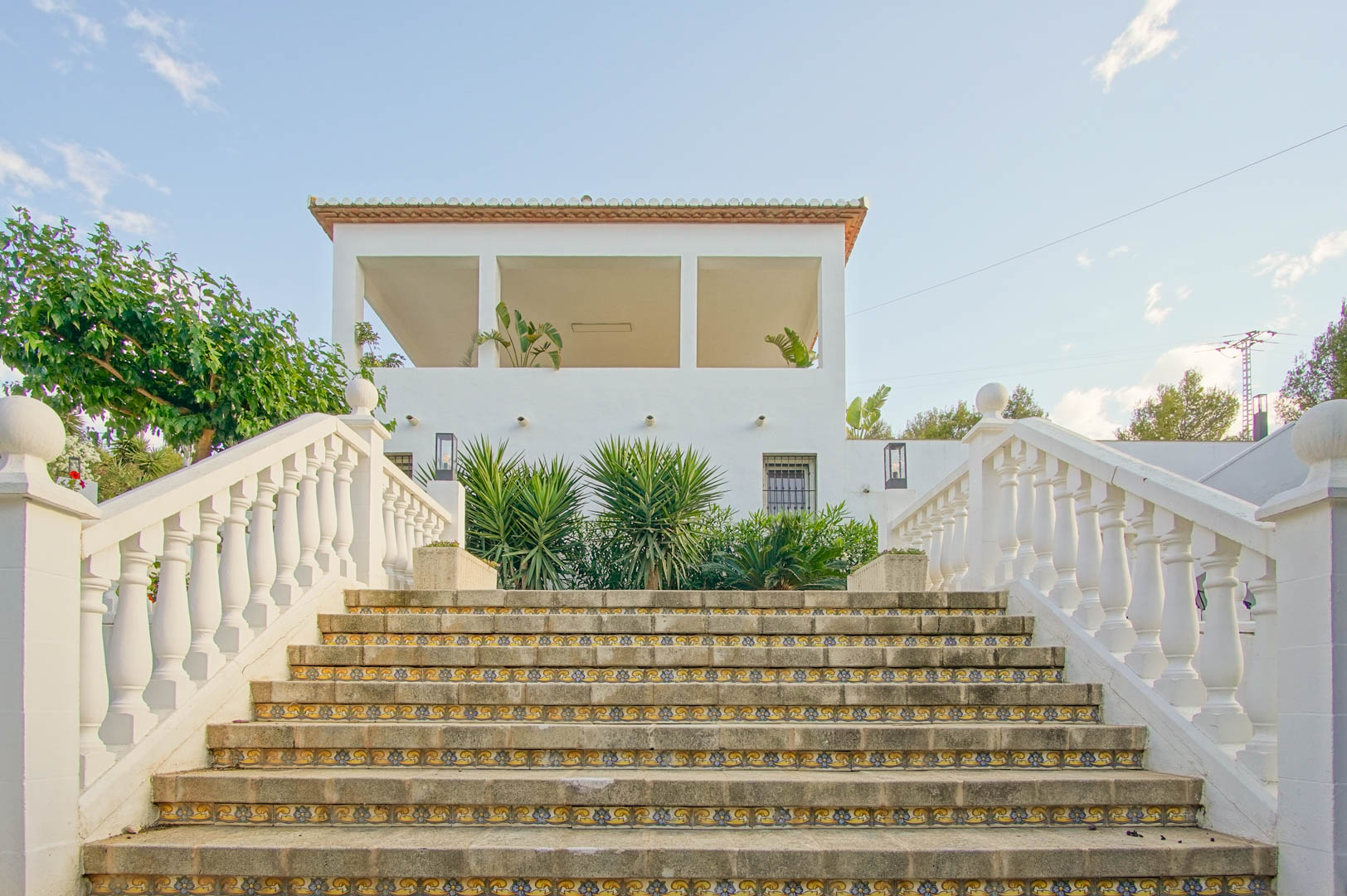 Außensteintreppe mit dekorativen Keramikfliesen an den Setzstufen und weißer Balustrade, die zur oberen Terrasse und der Villenfassade führt.