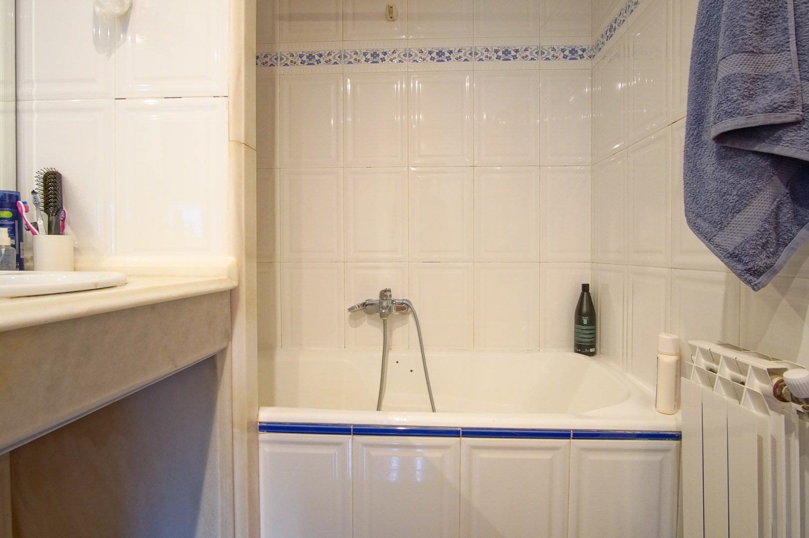 Badezimmer mit Badewanne, weißen Wandfliesen mit blauen floralen Akzenten und Marmor-Waschtischplatte. Inklusive Heizkörper und verchromter Mischbatterie.