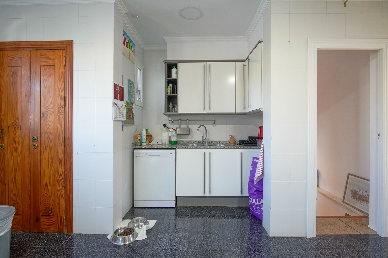 Funktionale Küche im Gästeapartment mit weißen Schränken, Granit-Arbeitsplatte und dunklem Terrazzoboden, direkt neben dem Zugang zu den oberen Etagen.