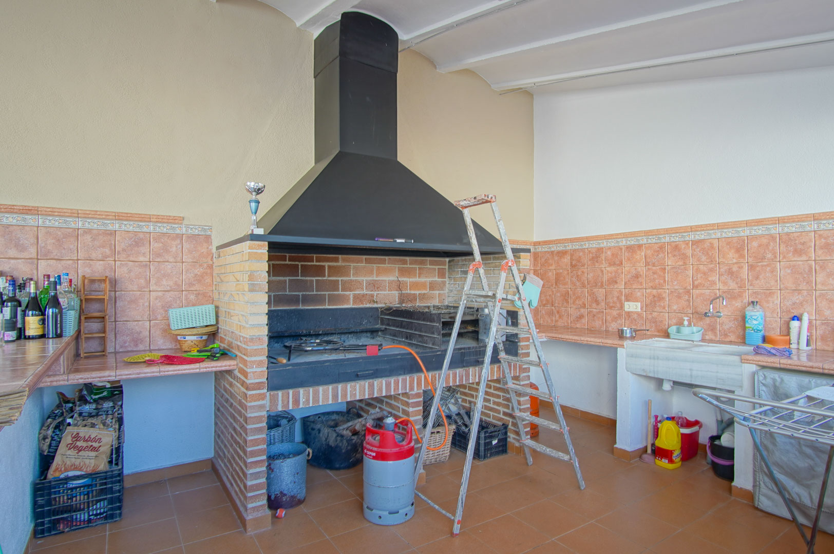 Gemauerter Grillbereich mit großer schwarzer Metallhaube, Steinspülbecken und terracottafarbenen Arbeitsplatten für die Bewirtung im Freien.