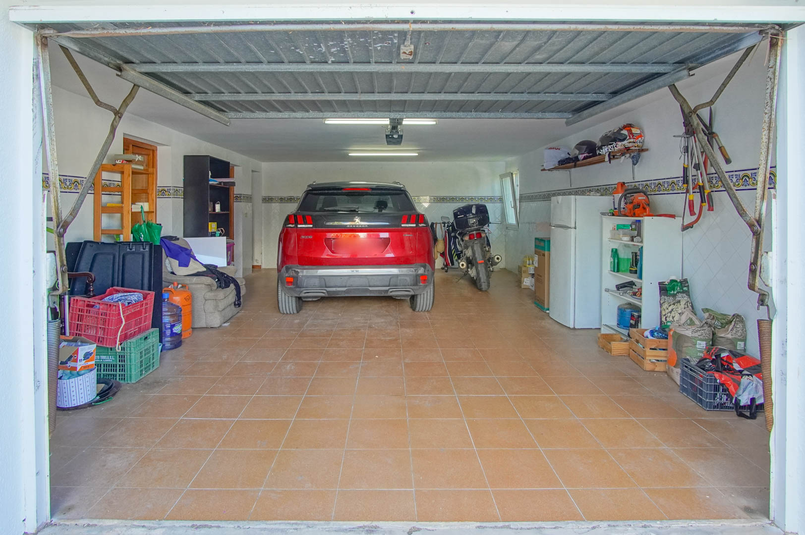 Geschlossene Garage im Souterrain mit Keramikfliesen, Leuchtstoffröhren und vielseitigem Platz für Fahrzeuge sowie Lagerung von Werkzeugen.