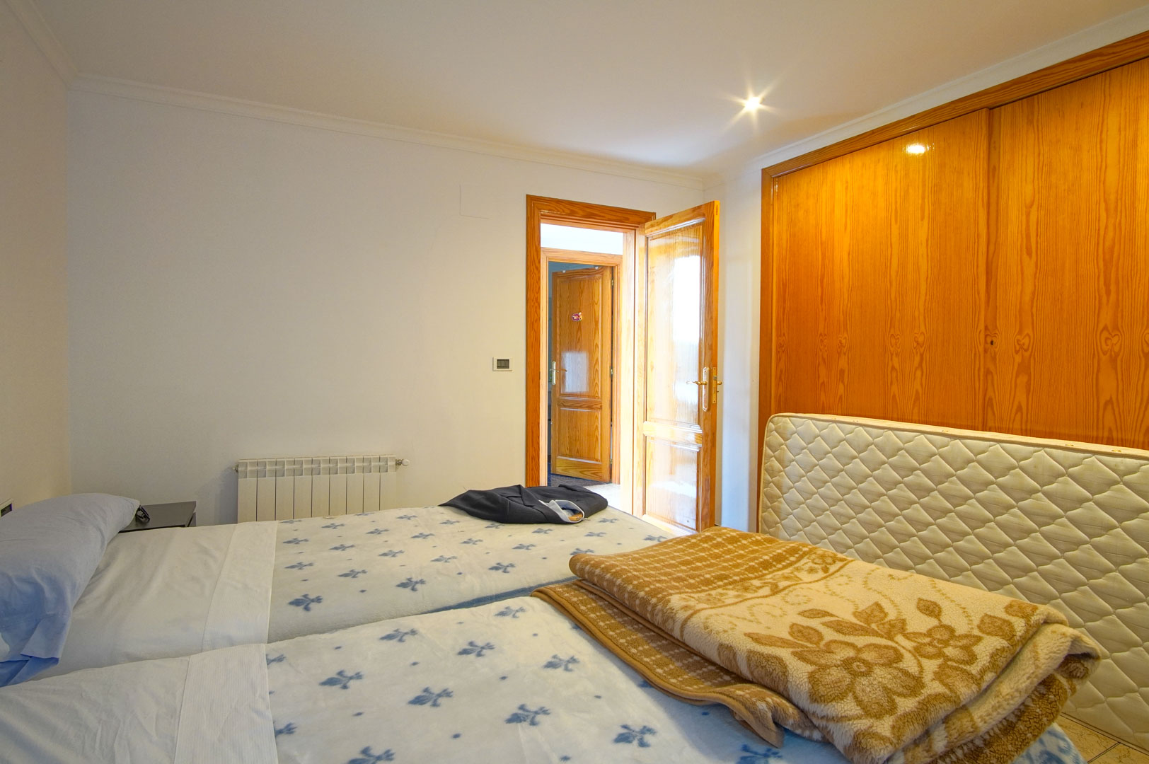 Helles Schlafzimmer mit großen Einbauschränken aus Holz, zwei Einzelbetten und Wandheizkörper. Passende Holztüren und Einbaustrahler sorgen für ein wohnliches Ambiente.