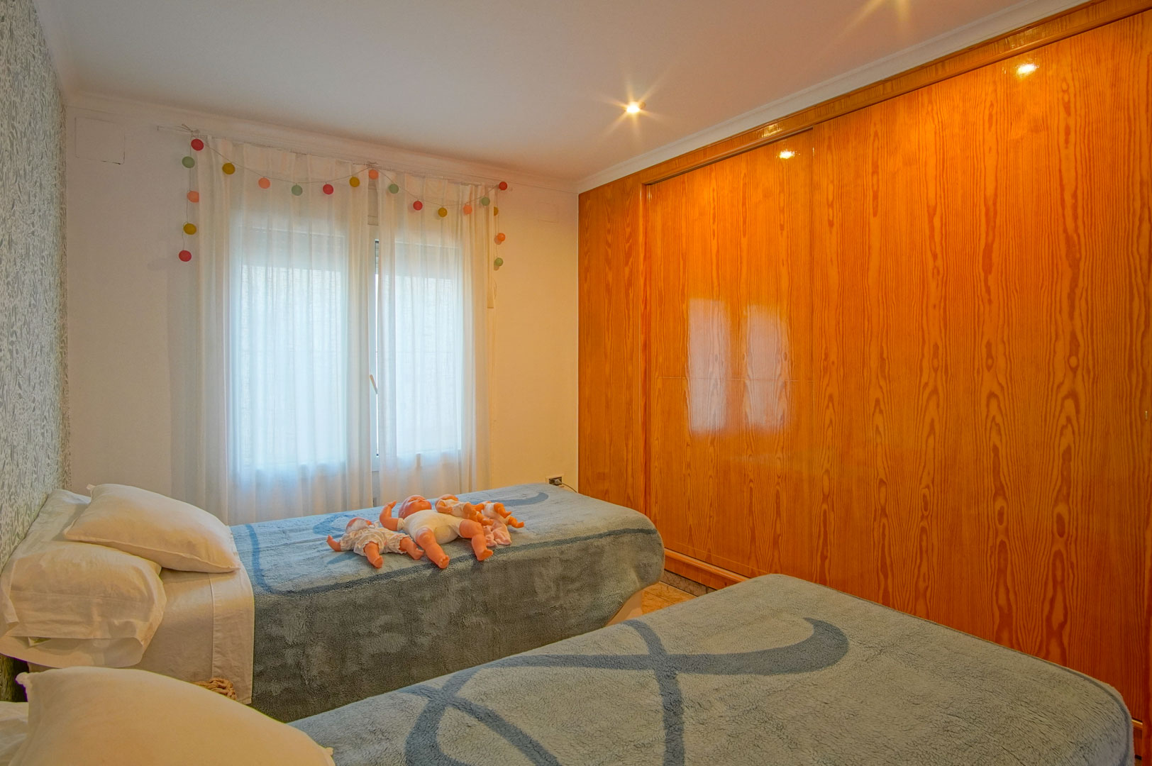 Helles Schlafzimmer mit zwei Einzelbetten, floraler Tapete und einem großen Einbauschrank aus Naturholz mit Glanzfinish.