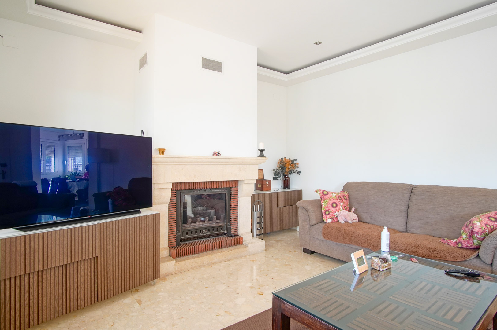 Helles Wohnzimmer mit einem Kamin aus Stein und Ziegeln, poliertem Marmorboden und maßgefertigten Holzschränken für den TV-Bereich.