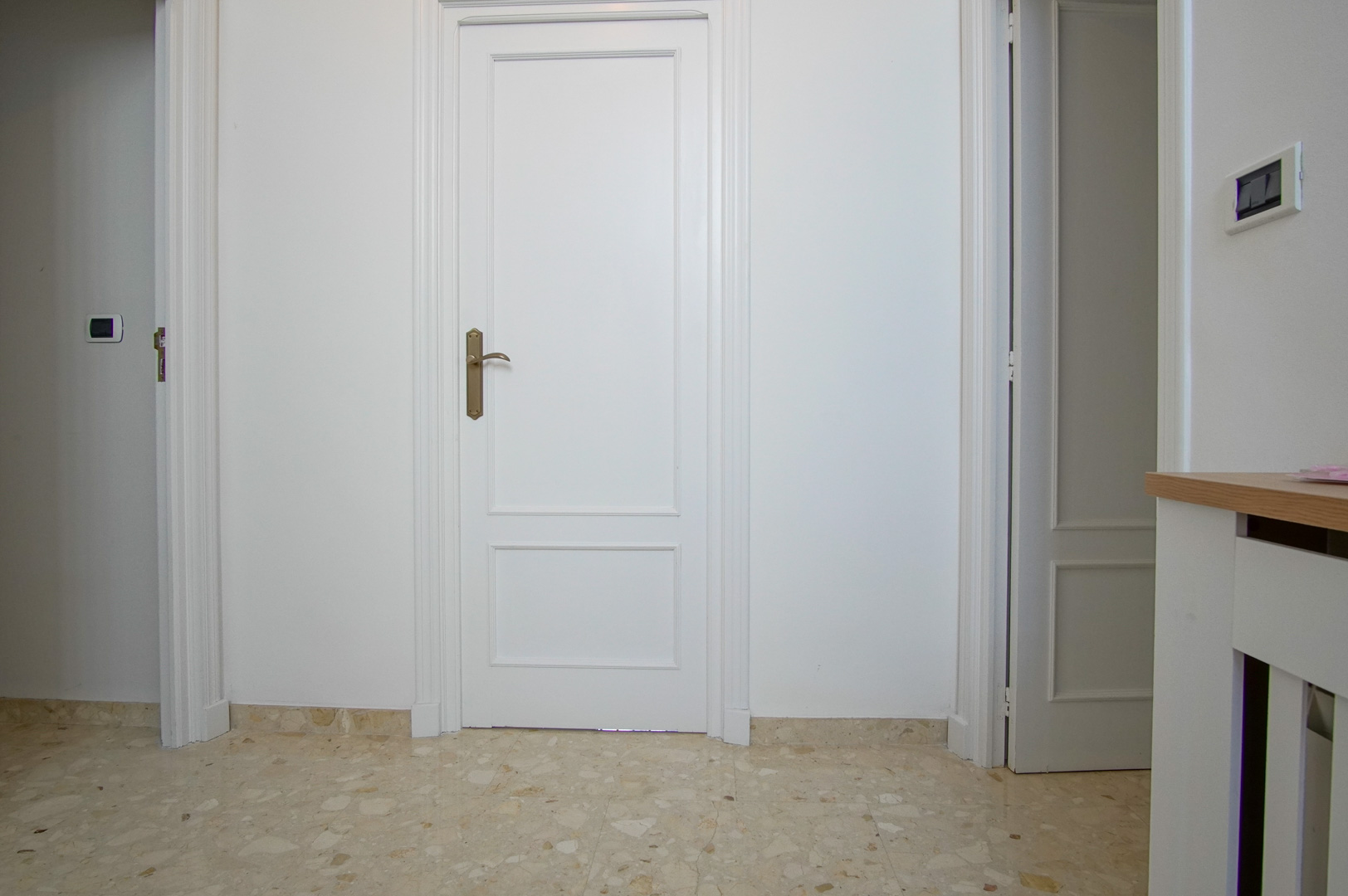 Innenflur mit weiß lackierten Kassettentüren und poliertem Marmorboden. Das klassische Design wird durch elegante Zierleisten und Beschläge in Bronzeoptik ergänzt.