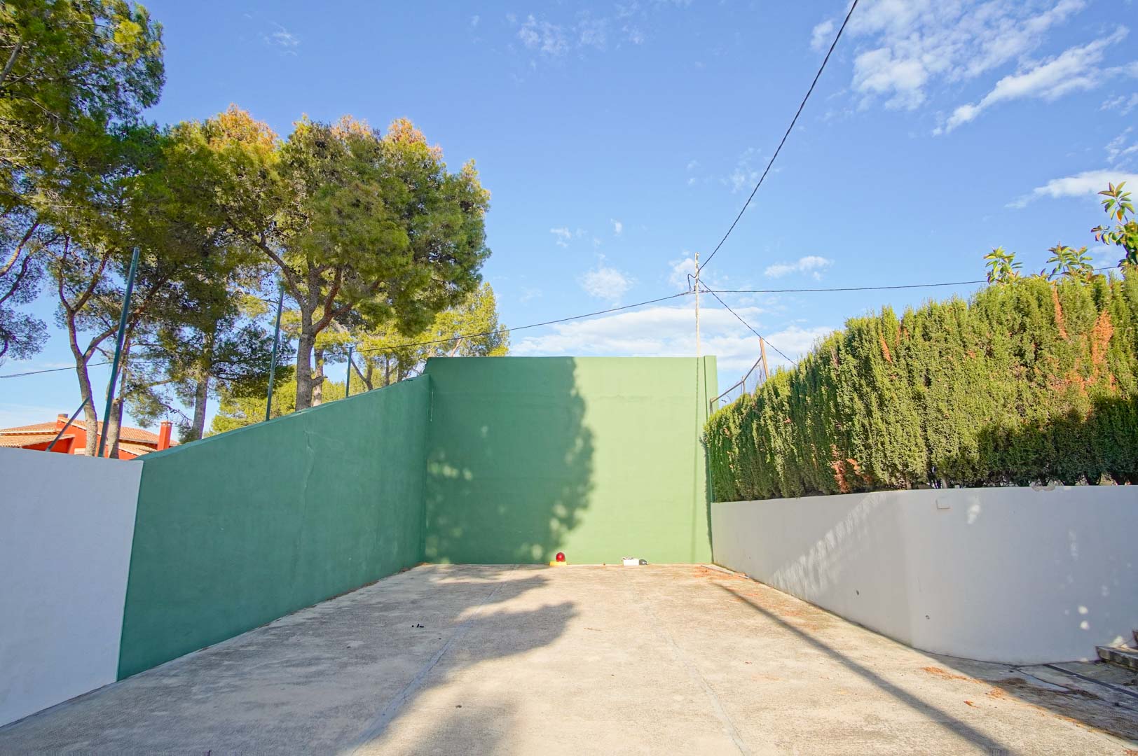 Privater Fronton-Platz mit grünen Wänden und Betonboden, umgeben von altem Baumbestand und hohen Hecken für optimale Privatsphäre.
