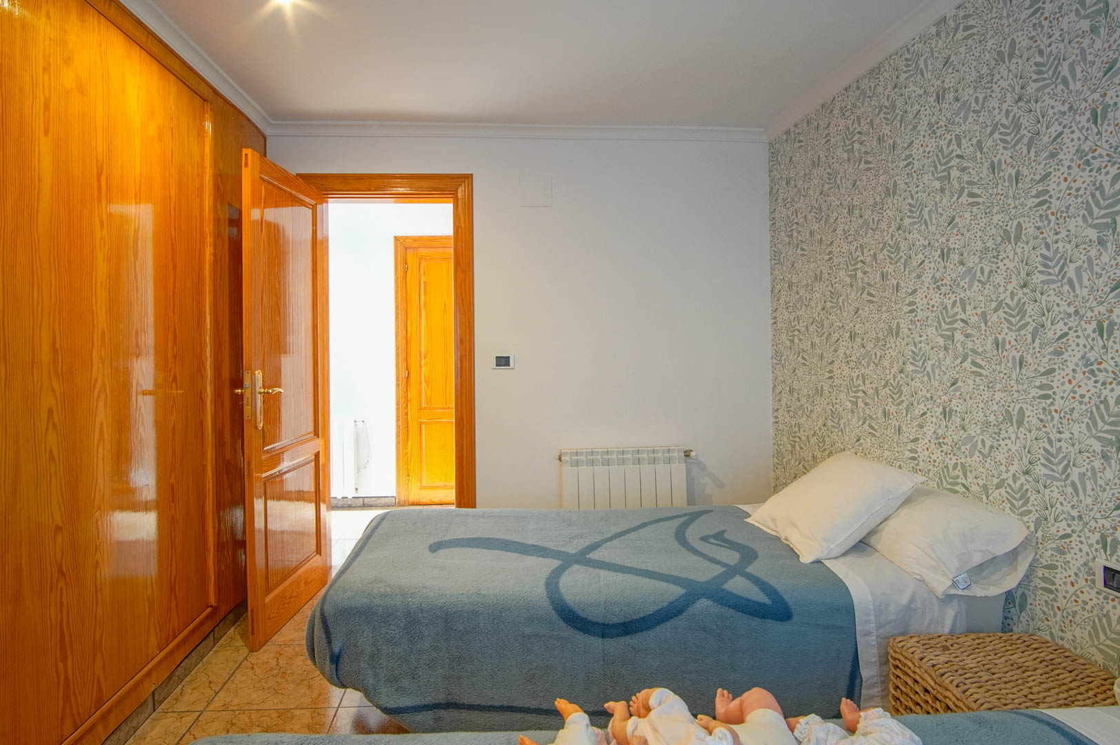 Schlafzimmer mit Einbauschrank aus poliertem Holz, botanischer Mustertapete, Fliesenboden und wandmontiertem Heizkörper.