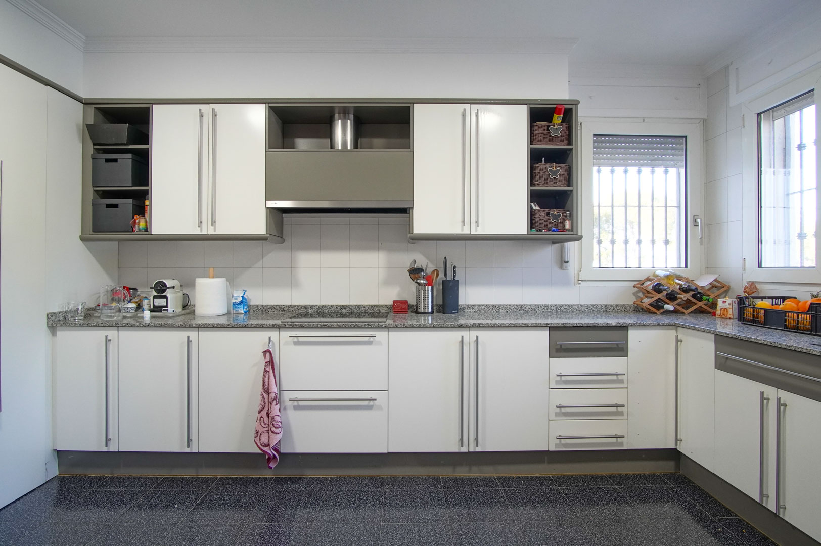 Separate Küche mit weißen Schränken, grauer Granitarbeitsplatte und Induktionskochfeld. Der dunkle, gesprenkelte Fliesenboden ergänzt das helle Design.