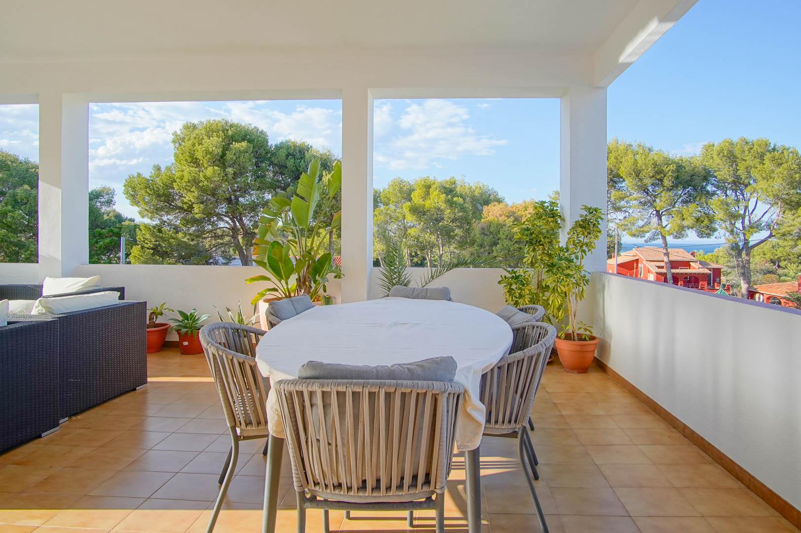 Überdachte Terrasse mit Essbereich und Lounge-Möbeln, die einen weiten Blick auf den mediterranen Pinienwald und den Meereshorizont bietet.