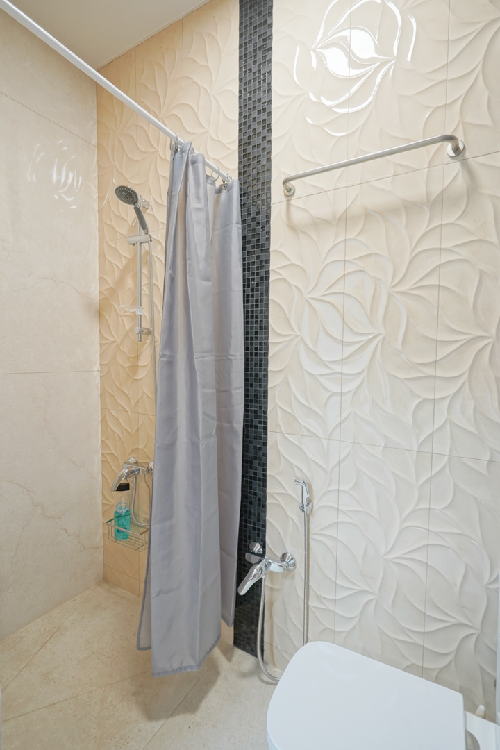 Badezimmer mit cremefarbenen Relief-Wandfliesen, einem vertikalen schwarzen Mosaikakzent und verchromten Armaturen.