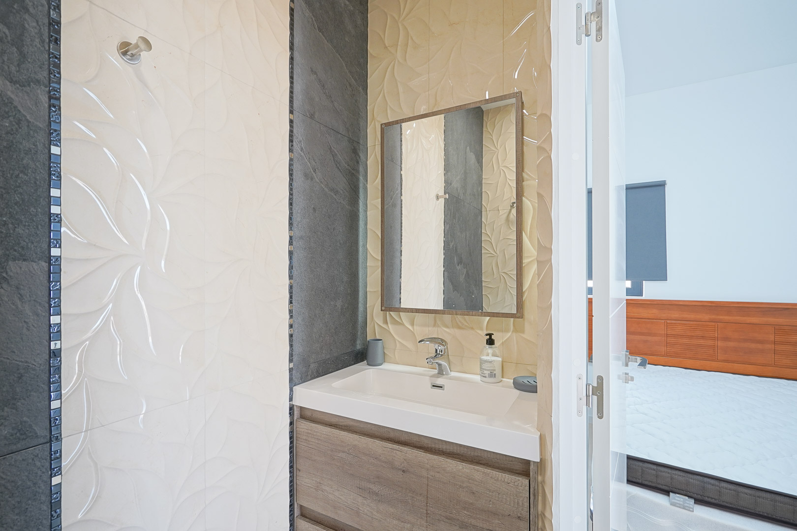 En-Suite-Badezimmer mit Holzwaschtisch, integriertem Waschbecken und dekorativen Relief-Wandfliesen mit dunklen Schieferakzenten.