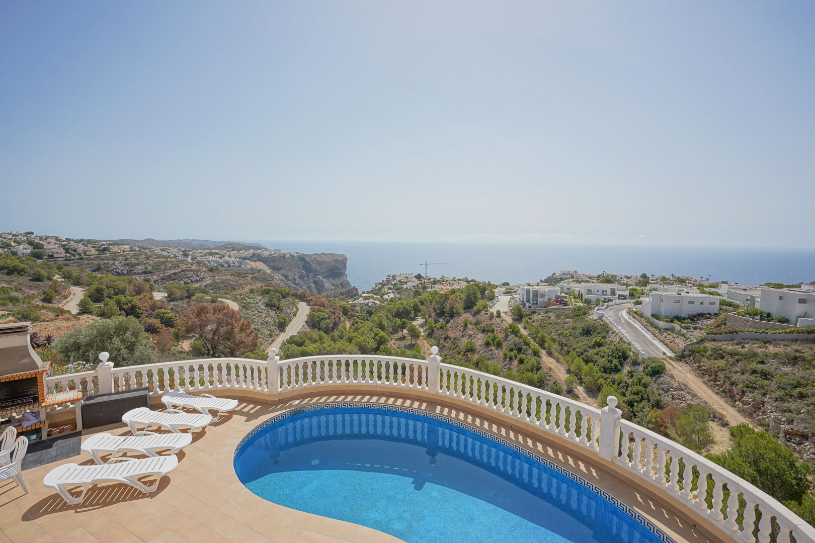 Erhöhte Terrasse mit nierenförmigem Pool, weißer Balustrade und gemauertem Grillbereich mit weitem Blick auf das Mittelmeer und die Klippen.