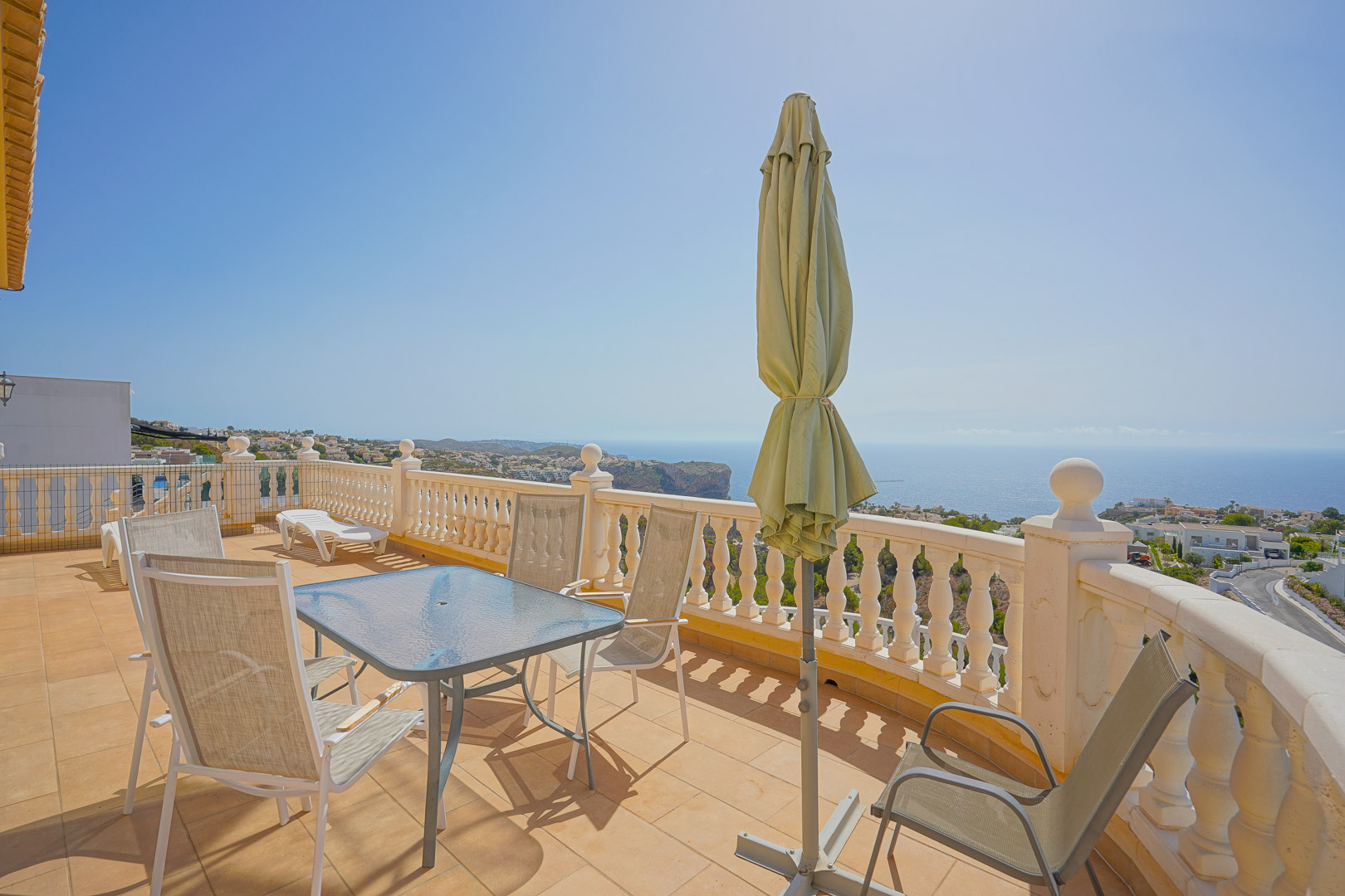 Obere Terrasse mit Glastisch, Außenbestuhlung und weißer Balustrade, die einen Panoramablick auf das Mittelmeer und die Klippen von Cumbre del Sol bietet.