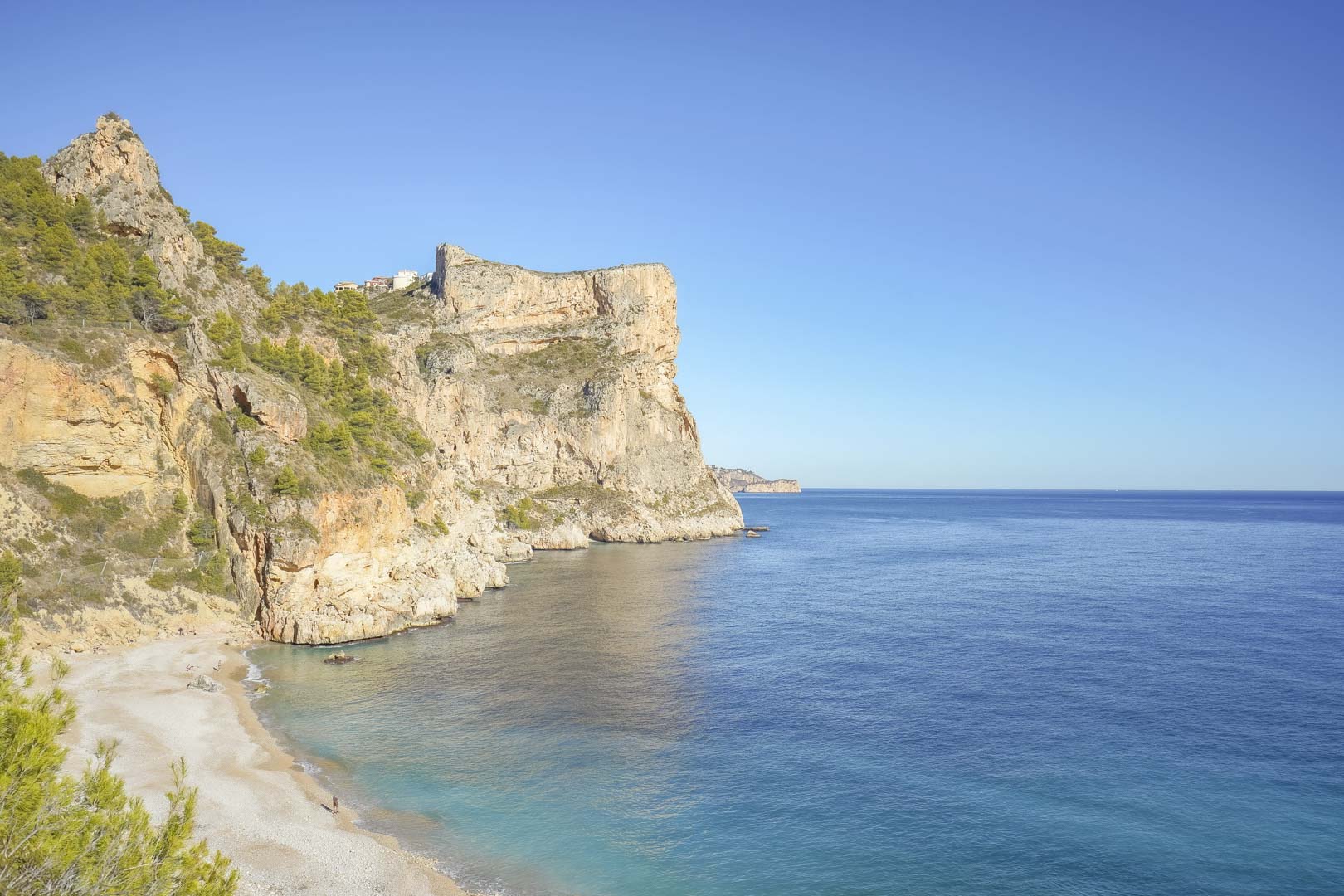 Panoramablick auf die Klippen von Cumbre del Sol und den Strand Cala Moraig mit dem tiefblauen Mittelmeer und markanten Kalksteinformationen.