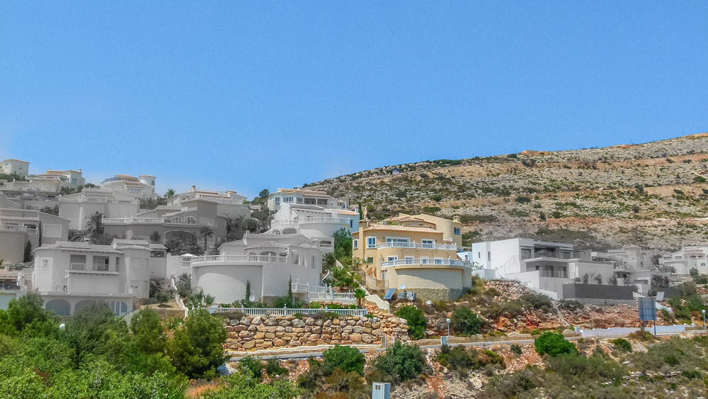 Panoramablick auf terrassenförmig angelegte weiße Villen am Hang von Cumbre del Sol mit Natursteinmauern und geschwungenen Balkonen.