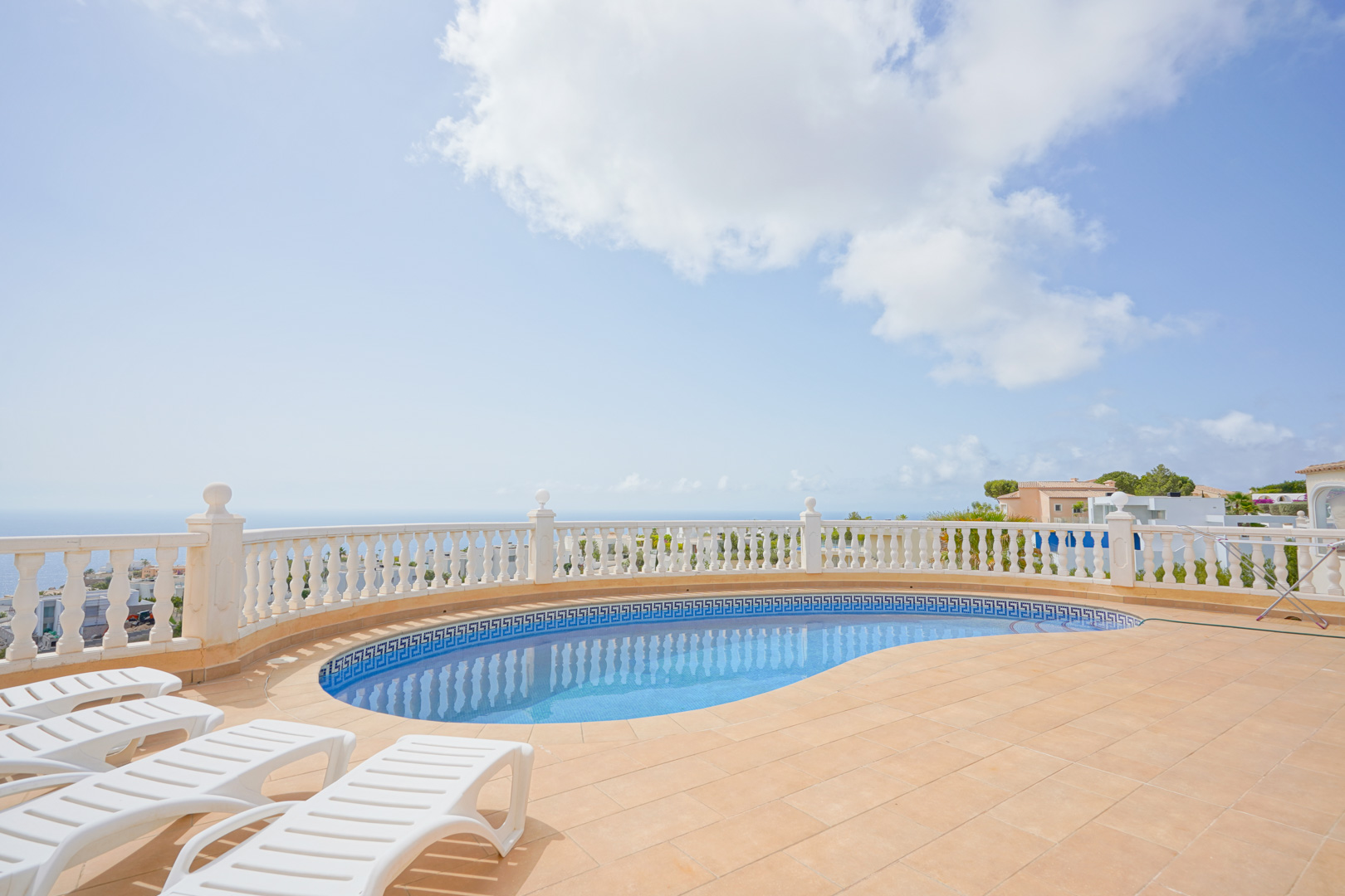 Terrasse mit geschwungenem Pool, weißer Balustrade und Panoramablick auf das Mittelmeer, ausgestattet mit Sonnenliegen auf Terrakottafliesen.