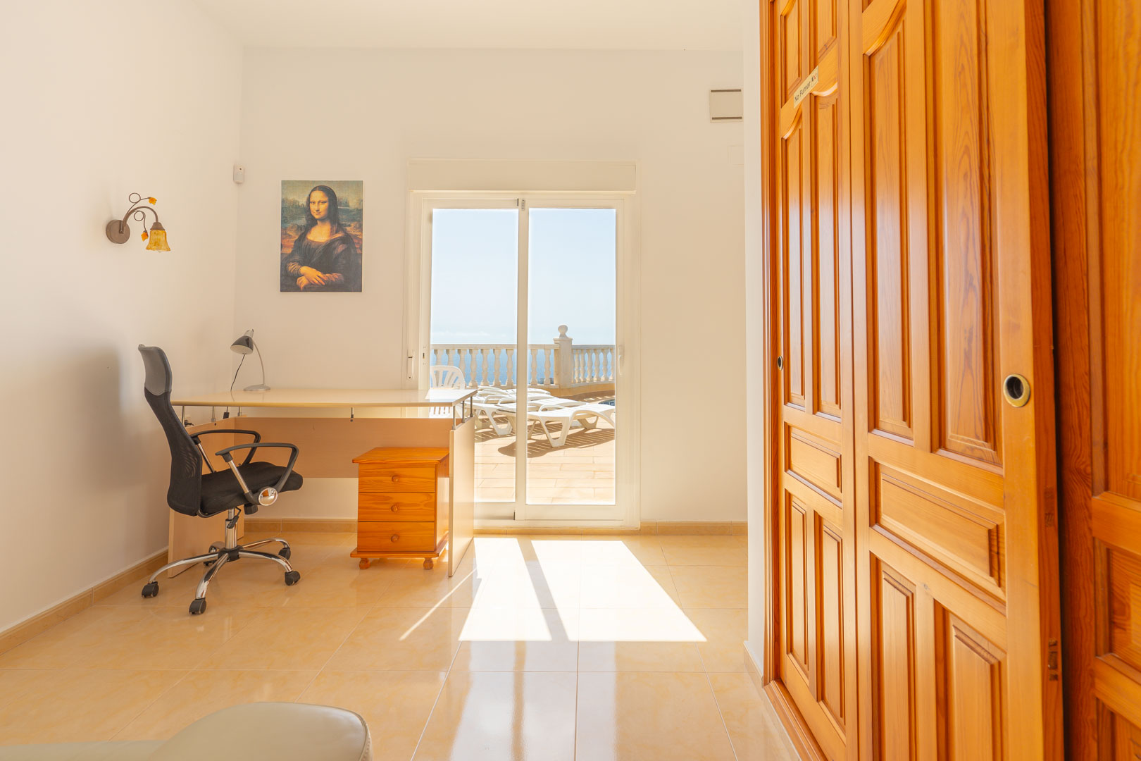 Vielseitiges Zimmer mit Arbeitsbereich, Einbauschränken aus Holz und direktem Zugang zur sonnigen Terrasse mit Meerblick durch Glasschiebetüren.