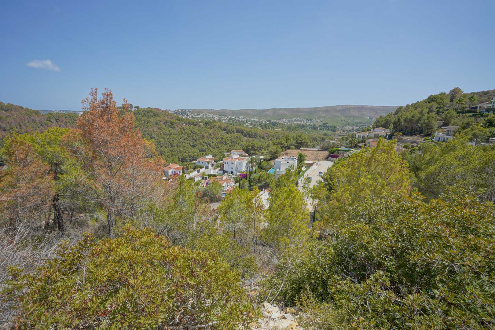 Erhöhter Blick vom Grundstück über das Tal mit mediterraner Vegetation und weißen Villen, die in die hügelige Landschaft eingebettet sind.