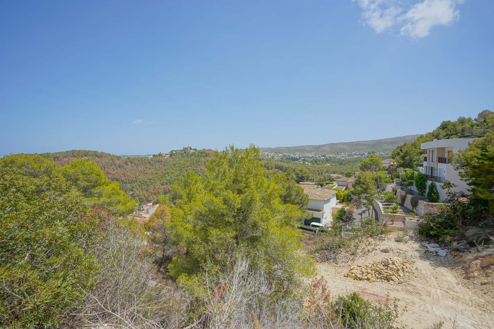 Panoramablick vom Hanggrundstück auf bewaldete Hügel und moderne Villen in einer neu erschlossenen, naturnahen Wohngegend.