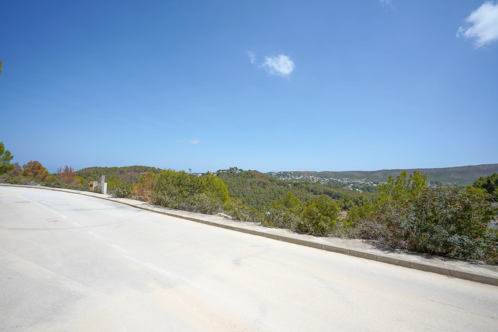 Panoramablick von der asphaltierten Zufahrtsstraße mit sichtbarer Infrastruktur und weitem Blick über die bewaldeten Hügel der Umgebung.