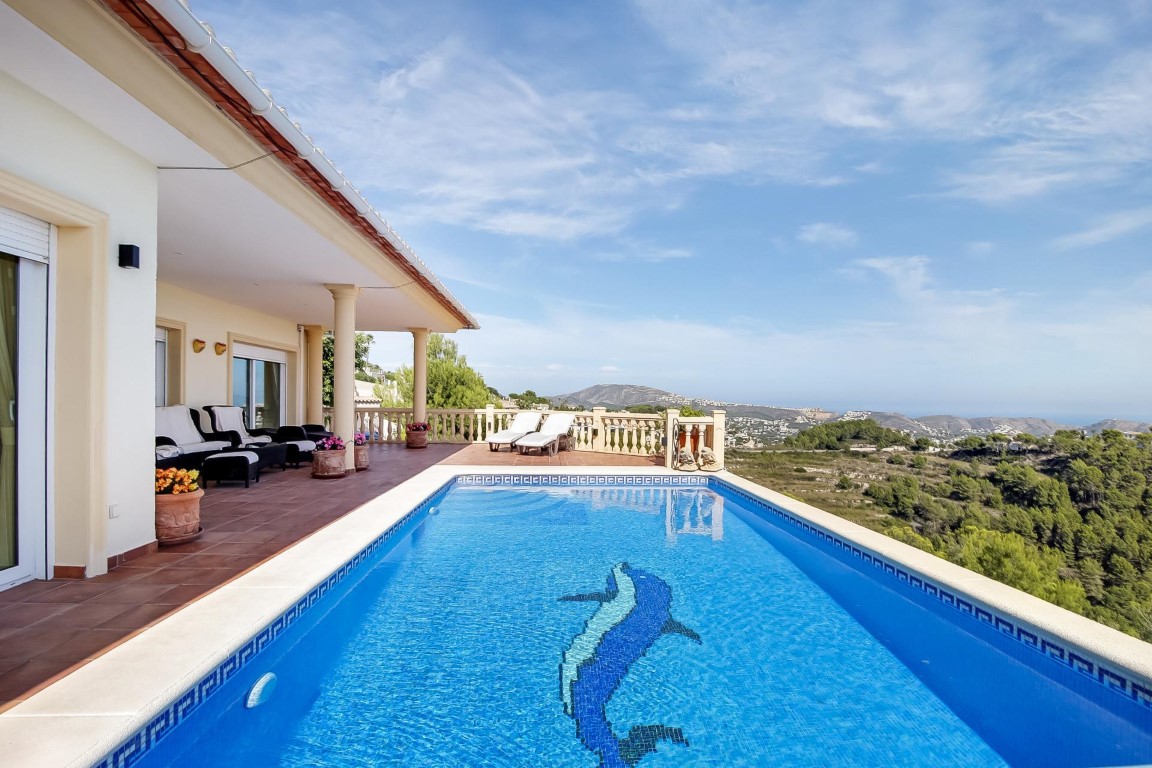 Außenpool mit Delfin-Mosaik und weitläufiger Terrakotta-Terrasse, die einen Panoramablick auf das Meer und die umliegende Landschaft von Moraira bietet.