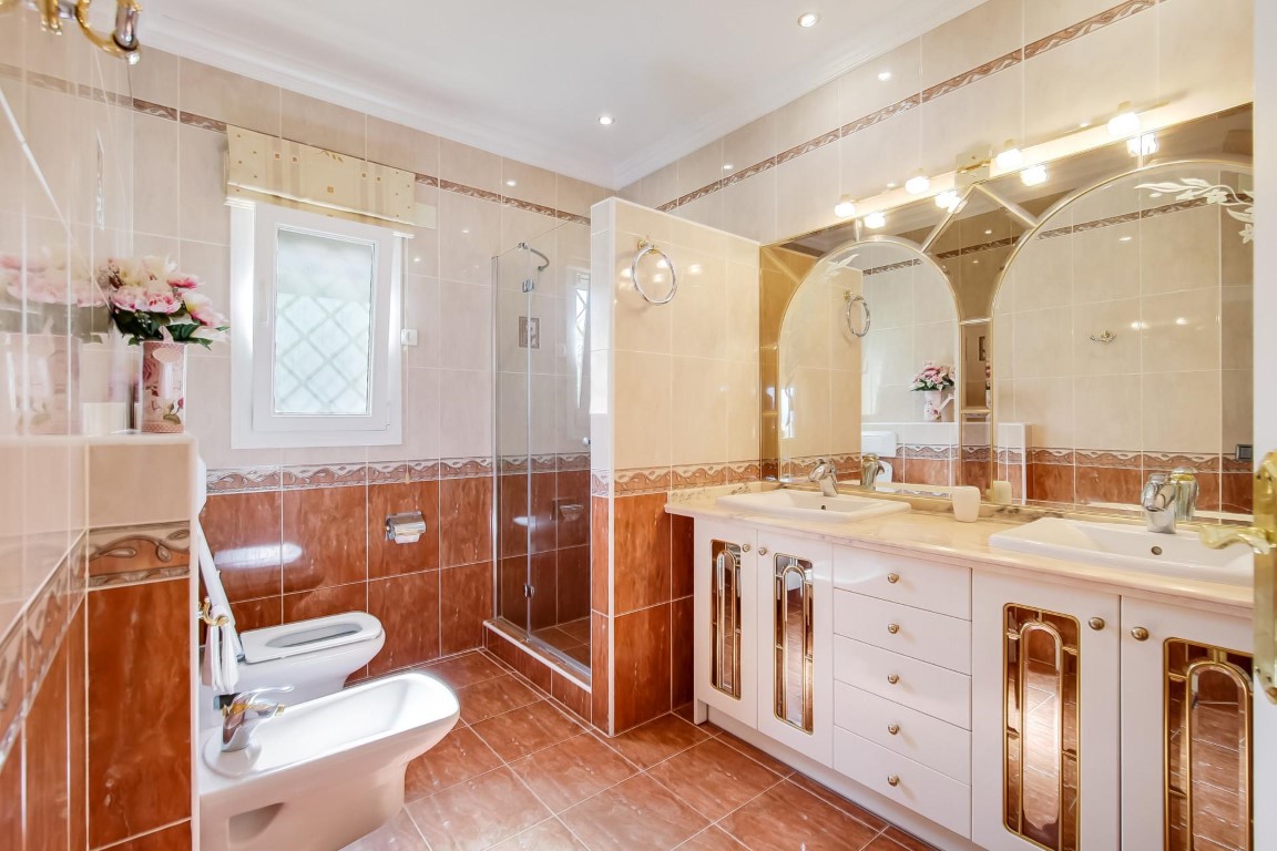 Komplettes Badezimmer mit Doppelwaschtisch, bogenförmigen Spiegeln mit integrierter Beleuchtung und einer begehbaren Glasdusche.