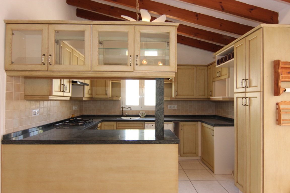 Rustikale Küche mit sichtbaren Holzbalken, dunklen Granitarbeitsplatten und cremefarbenen Schränken mit Glasfronten sowie einer praktischen Frühstückstheke.