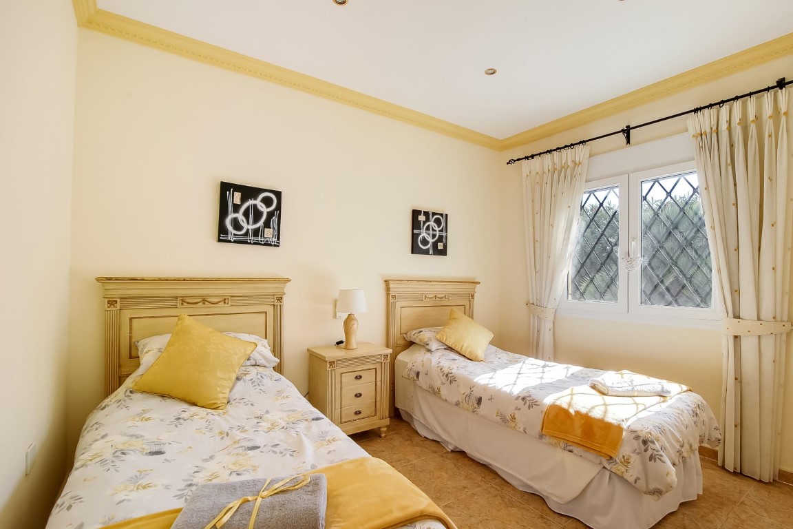 Schlafzimmer mit zwei klassischen Einzelbetten aus Holz, dekorativen Deckenleisten und einem Fenster mit traditionellen rautenförmigen Sicherheitsgittern.
