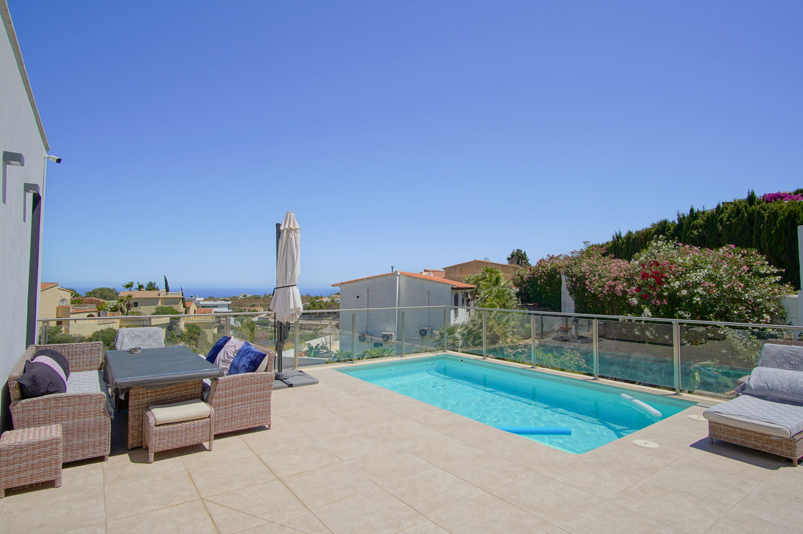 Außen-Terrasse mit rechteckigem Pool, Glasgeländer und Rattanmöbeln. Die nach Süden ausgerichtete Fläche bietet einen weiten Meerblick und viel Sonnenlicht.