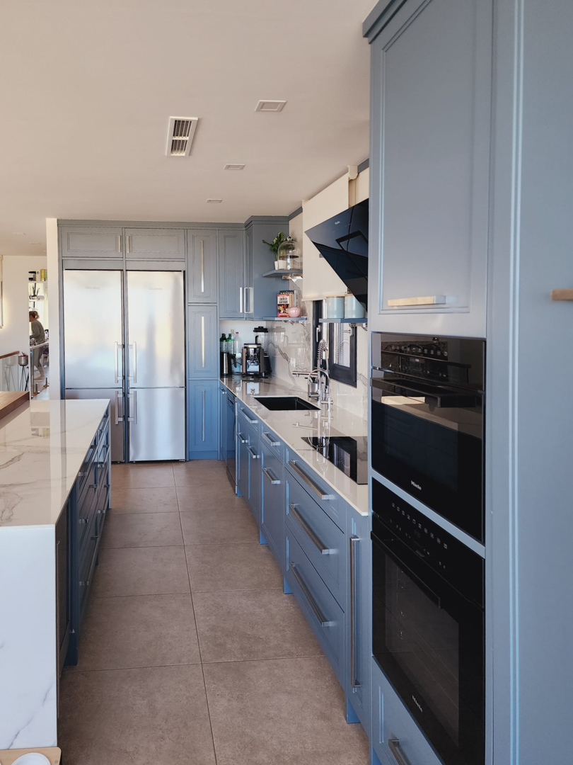 Designerküche mit blaugrauen Schränken, Arbeitsplatten in Marmoroptik und integrierten Miele-Geräten, einschließlich Doppelöfen und einem großen Edelstahlkühlschrank.
