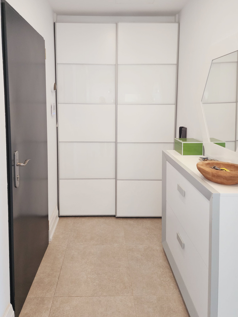 Eingangsbereich mit weißem Einbauschrank mit Schiebetüren, einer modernen Kommode und hellen Bodenfliesen in Natursteinoptik.