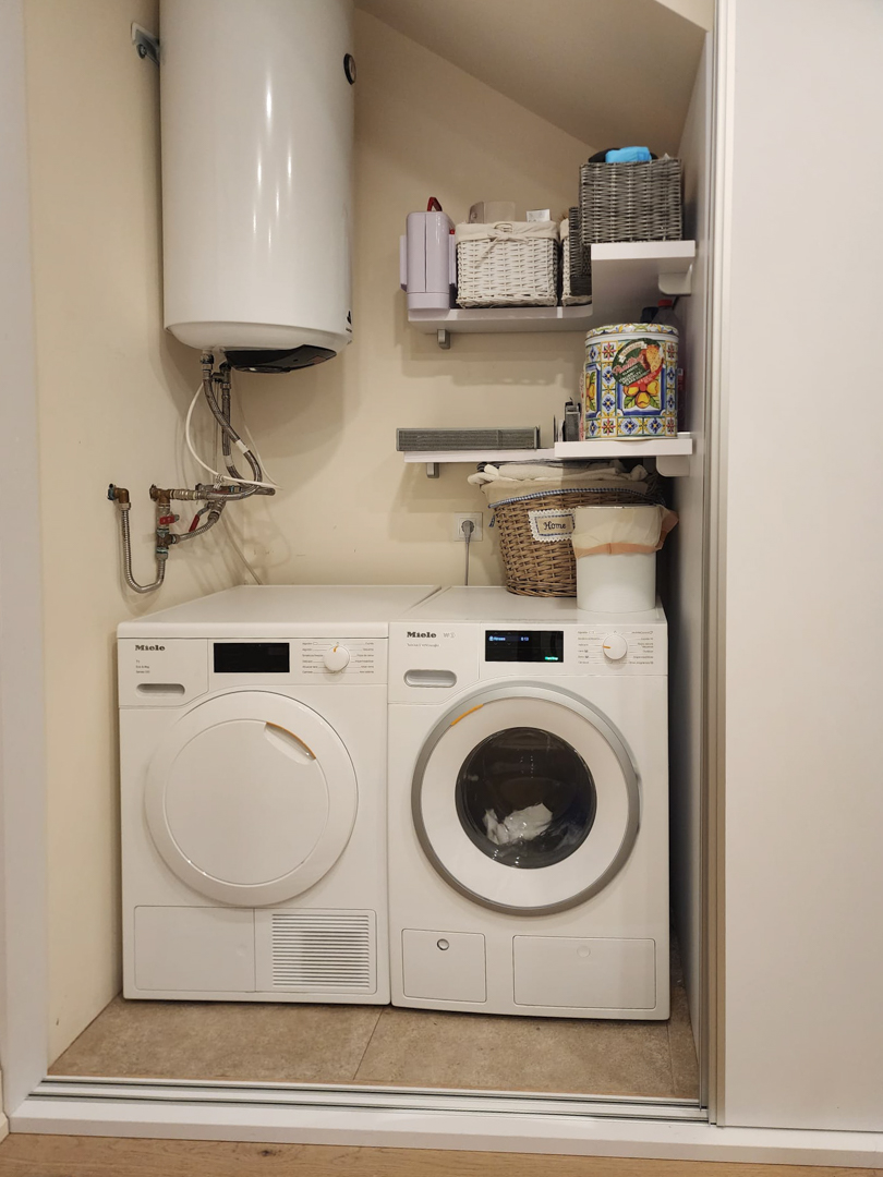 Hauswirtschaftsbereich mit Miele-Waschmaschine und -Trockner, Solar-Warmwasserspeicher und praktischen Regalen zur Aufbewahrung.