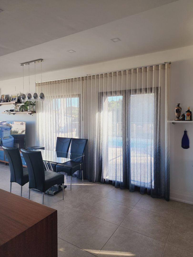 Heller Essbereich mit Glastisch und Hochlehner-Stühlen vor großen Fensterfronten mit Farbverlauf-Vorhängen und direktem Zugang zur Terrasse am Pool.