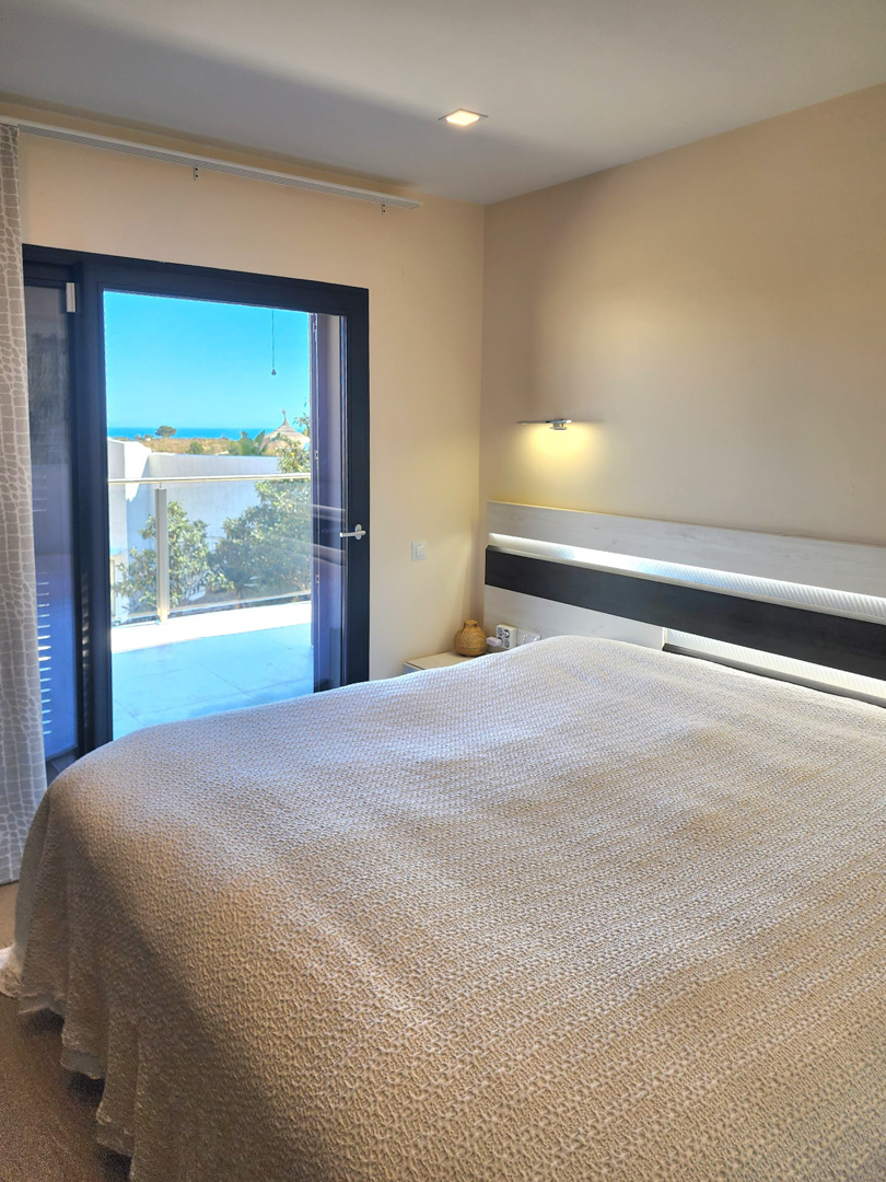 Helles Schlafzimmer mit integriertem LED-Kopfteil und direktem Zugang zur Terrasse mit Panoramablick auf das Mittelmeer.