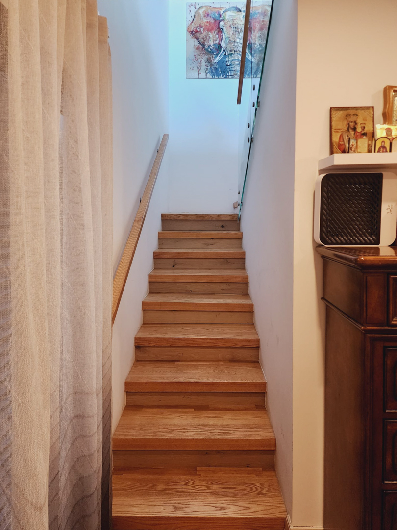 Innenliegende Holztreppe mit passendem Handlauf und Glasbalustrade, die durch natürliches Oberlicht erhellt und mit Wandkunst dekoriert ist.