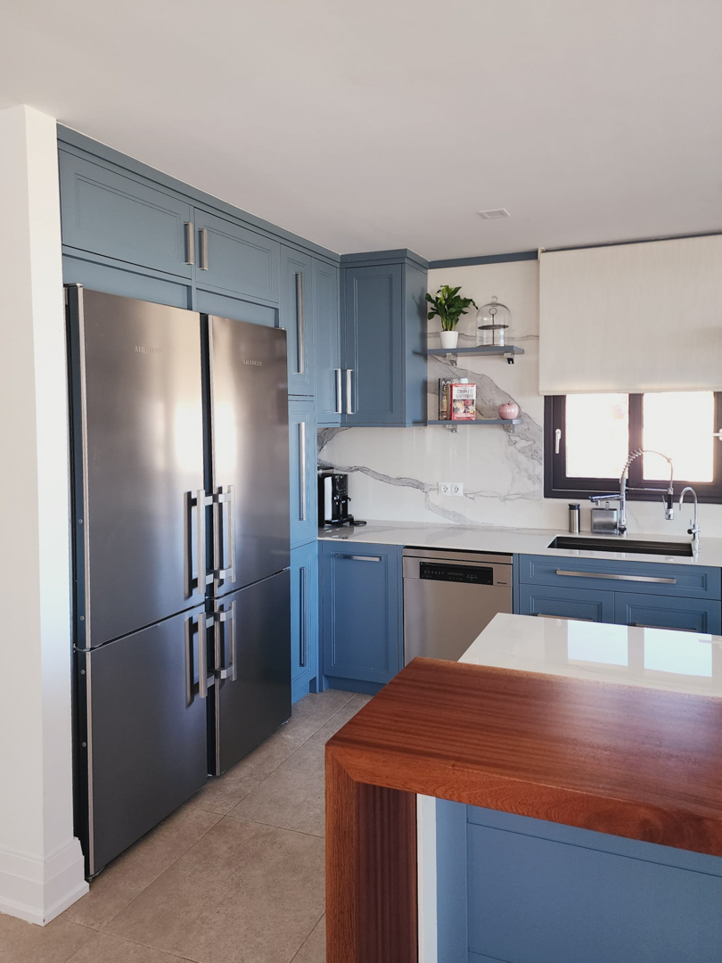 Moderne Küche mit blauen Fronten, Marmor-Rückwand und hochwertigen Edelstahlgeräten. Eine Frühstücksbar aus Echtholz setzt einen natürlichen Akzent.