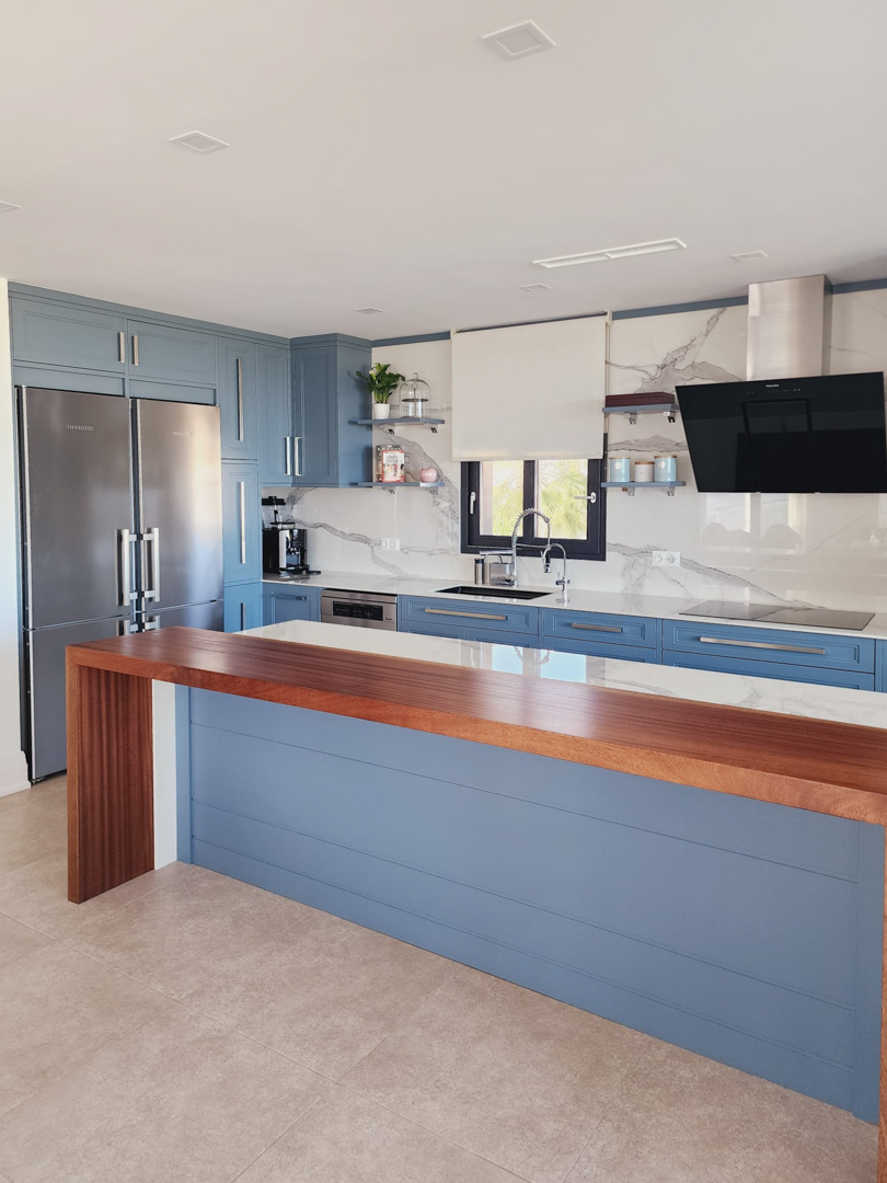Moderne Küche mit blauen Schränken, Arbeitsplatten in Marmoroptik und einer Massivholzbar. Sie bietet integrierte Geräte und einen großzügigen, hellen Arbeitsbereich.
