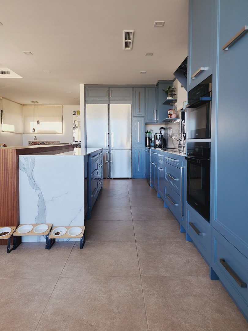 Moderne Küche mit pastellblauen Schränken, einer marmorierten Mittelinsel und integrierten Miele-Geräten. Feinsteinzeugboden und Klimaanlage über Deckenkanäle.