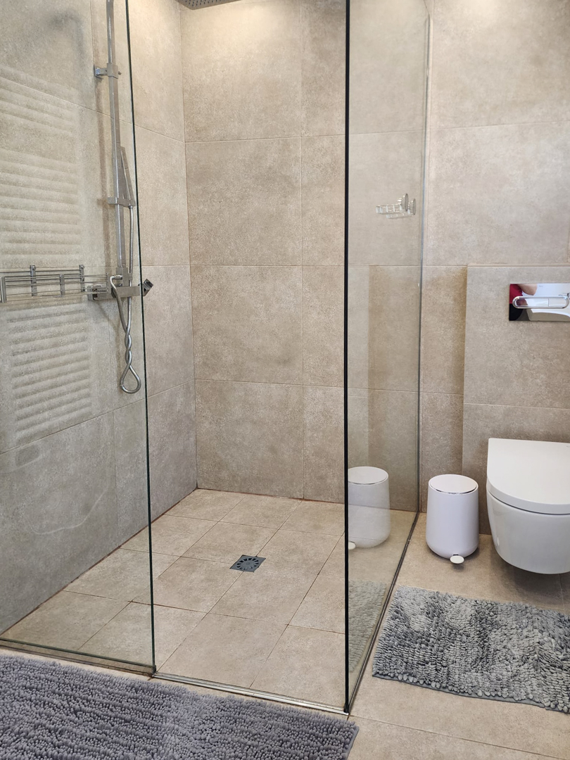 Modernes Badezimmer mit begehbarer Dusche, Glastrennwand und sandfarbenen Feinsteinzeugfliesen. Ausgestattet mit einem Wand-WC und verchromten Armaturen.