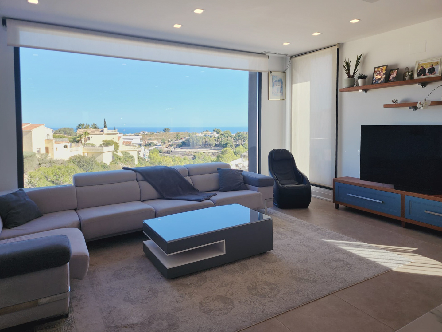 Modernes Wohnzimmer mit großem Panoramafenster und Meerblick, grauem Ecksofa, Design-Couchtisch und Deckeneinbaustrahlern.