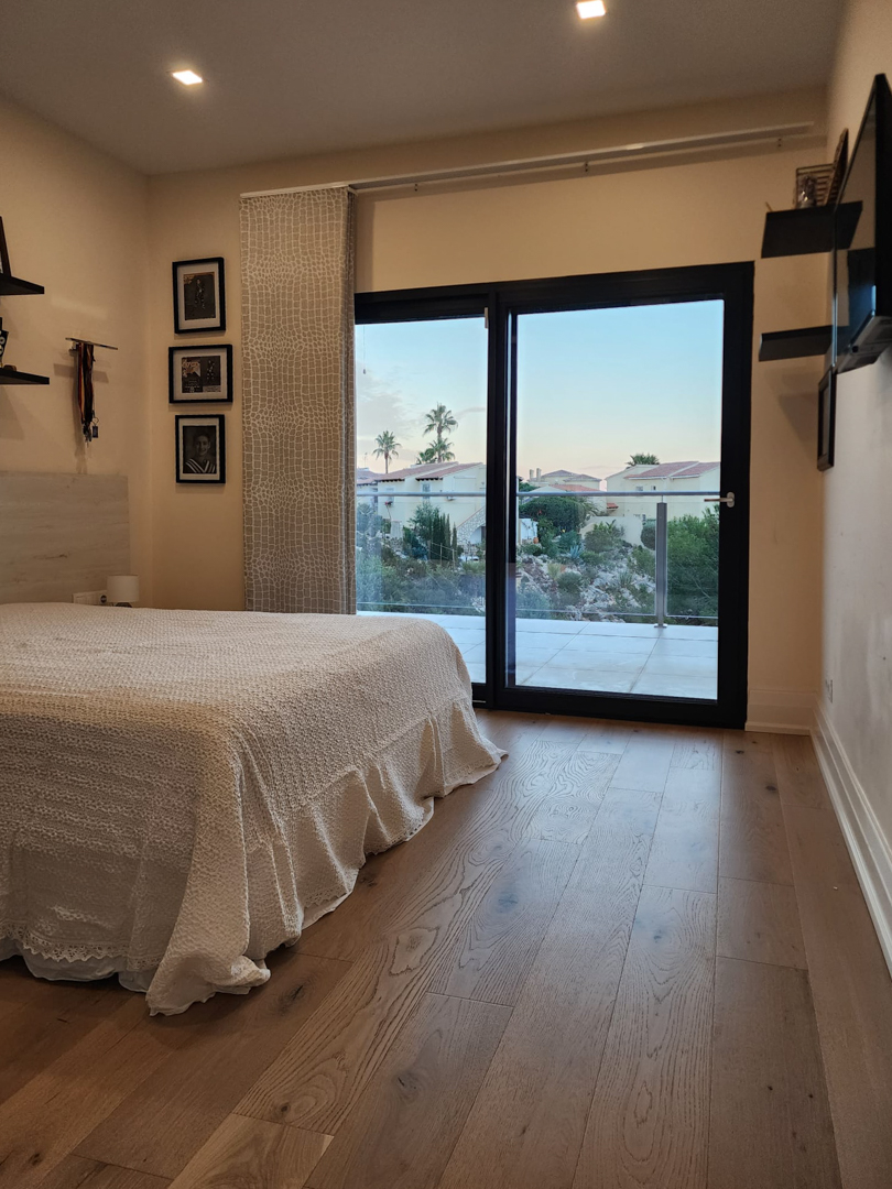Schlafzimmer mit Echtholzboden, Deckeneinbaustrahlern und großen Glasschiebetüren, die direkten Zugang zur Terrasse und Blick auf die Umgebung bieten.