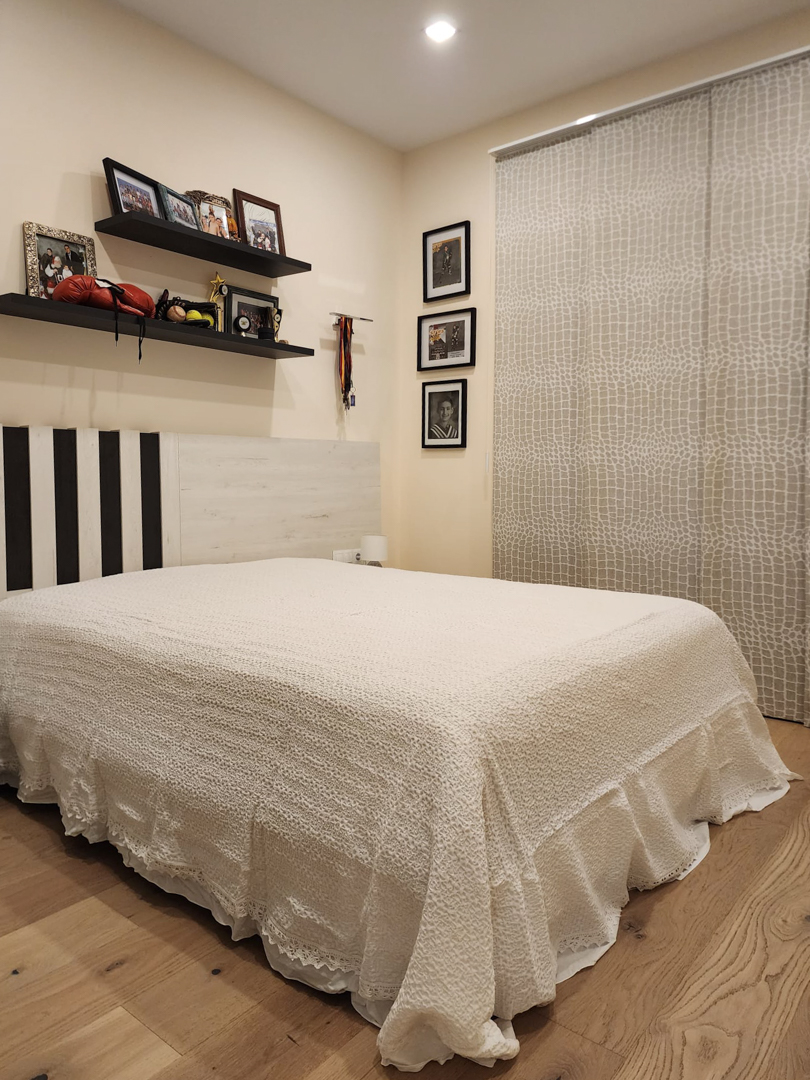 Schlafzimmer mit hellem Eichenparkett, modernem Kopfteil und Wandregalen. Ausgestattet mit gemusterten Flächenvorhängen und Deckeneinbaustrahlern.