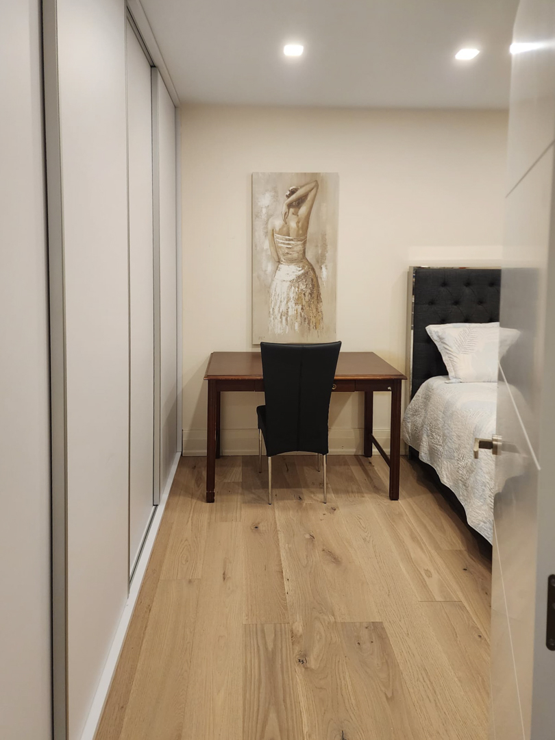 Schlafzimmer mit raumhohen Einbauschränken, einem Holzschreibtisch und Eichenparkettboden, beleuchtet durch dezente Deckeneinbaustrahler.