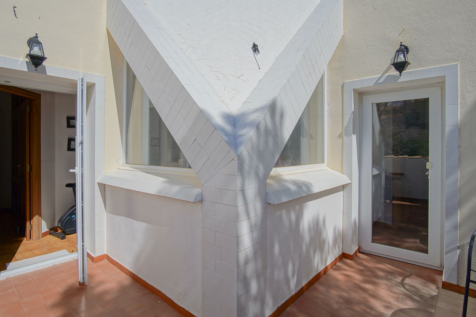 Architektonisches Detail der oberen Terrasse mit weiß gefliesten Säulen, Terrakottaboden und direktem Zugang zu den hellen Innenräumen.