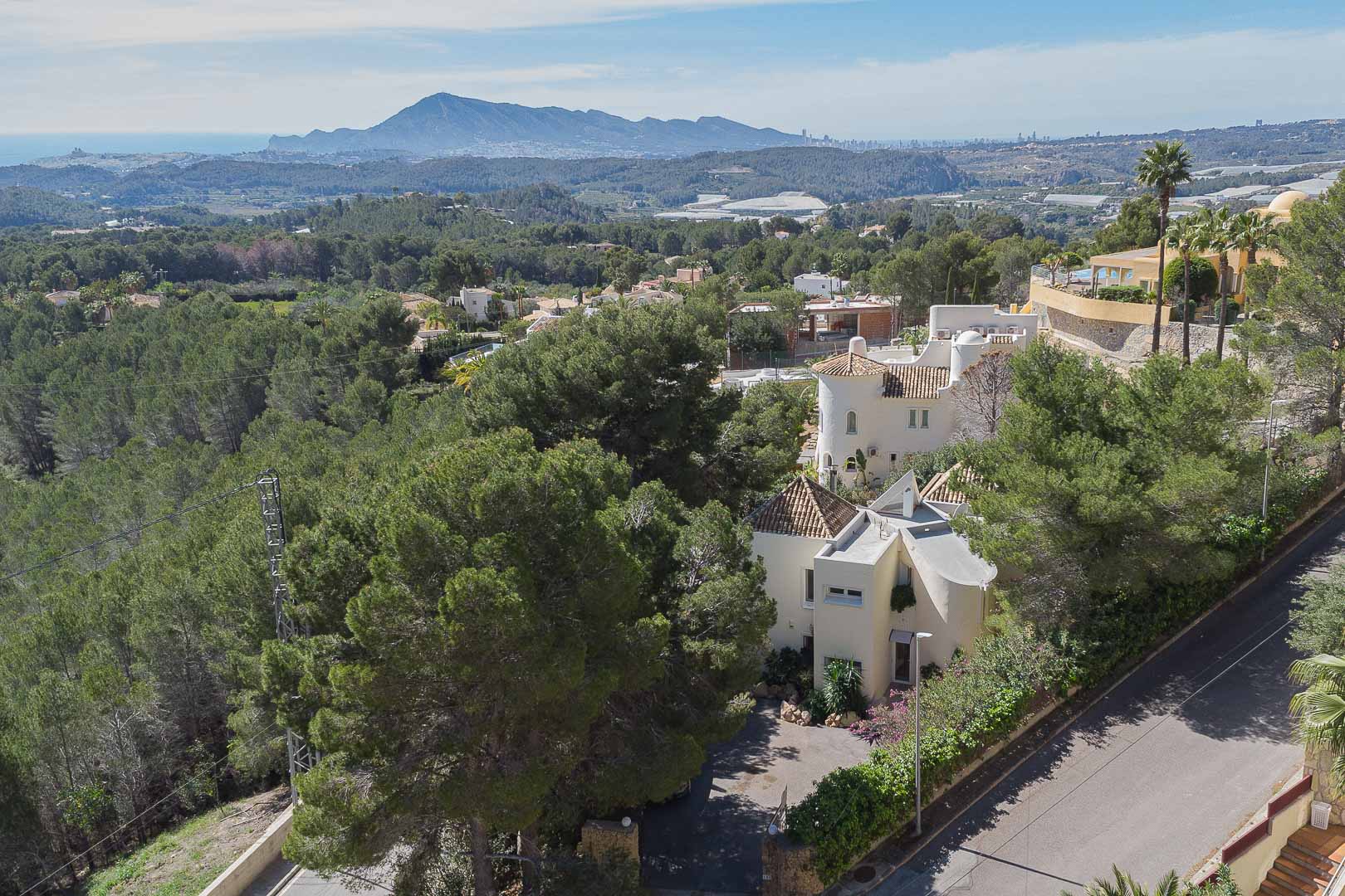 Erhöhte Ansicht der Villa inmitten eines Pinienwaldes, die die mediterrane Architektur sowie den weiten Blick auf das Meer und die umliegenden Berge zeigt.