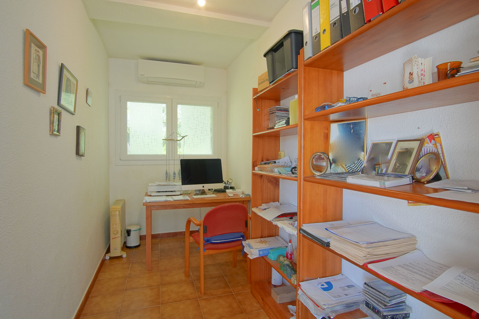 Funktionales Arbeitszimmer mit Holzschreibtisch, Wandregalen, Terrakotta-Fliesenboden und Klimaanlage, ideal für das Home-Office.