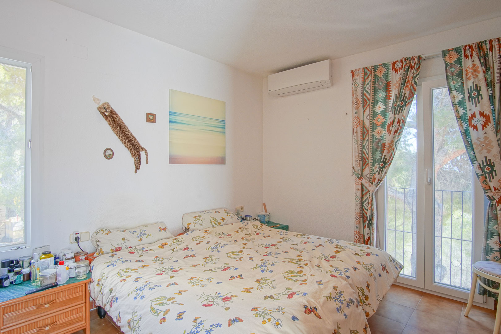 Helles Schlafzimmer mit Split-Klimaanlage, direktem Terrassenzugang durch Glastüren und rustikalen Fliesenböden.