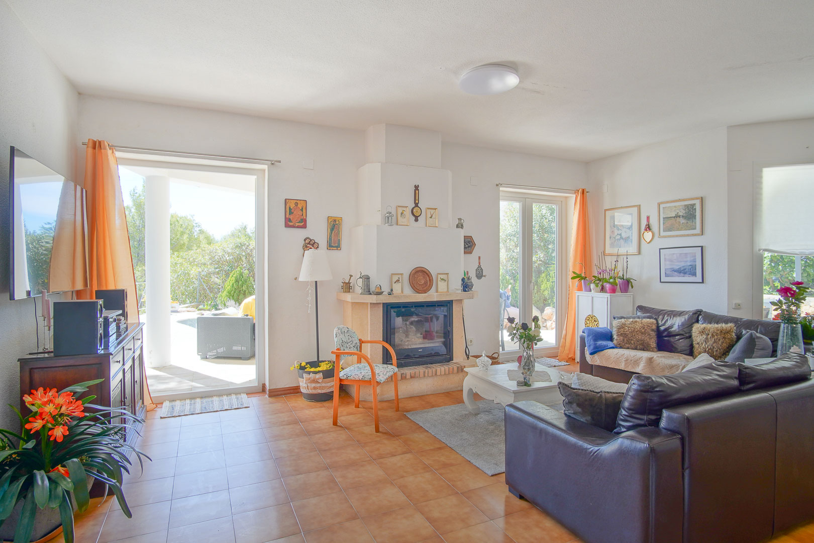 Helles Wohnzimmer mit zentralem Kamin, Terrakotta-Fliesenboden und direktem Zugang zur Außenveranda durch große Glastüren.